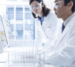 Scientists are looking at data charts on a computer with test tubes beside them.