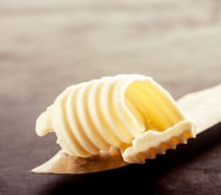 Curl of butter on a butter knife resting on a dark surface.