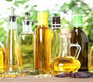 Assorted bottles of cooking oils with olives and herbs on a wooden surface.