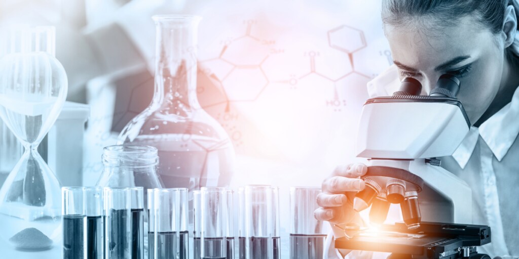 Scientist using a microscope with test tubes and lab glassware in a research setting