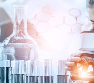 Scientist using a microscope with test tubes and lab glassware in a research setting