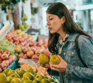 Woman selecting apples at a grocery store produce section, examining their quality.