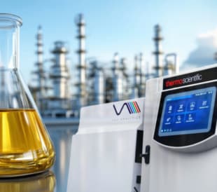 Flask with yellow liquid beside Thermo Scientific gas chromatograph in an industrial setting.