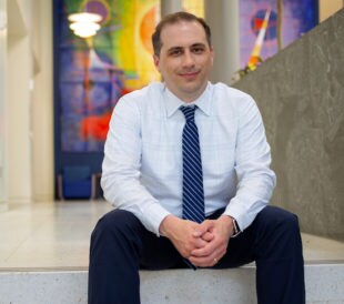 Dr. Philip Empey, who studies pharmacogenetics testing with clinical care, sits on the steps of a modern building interior.