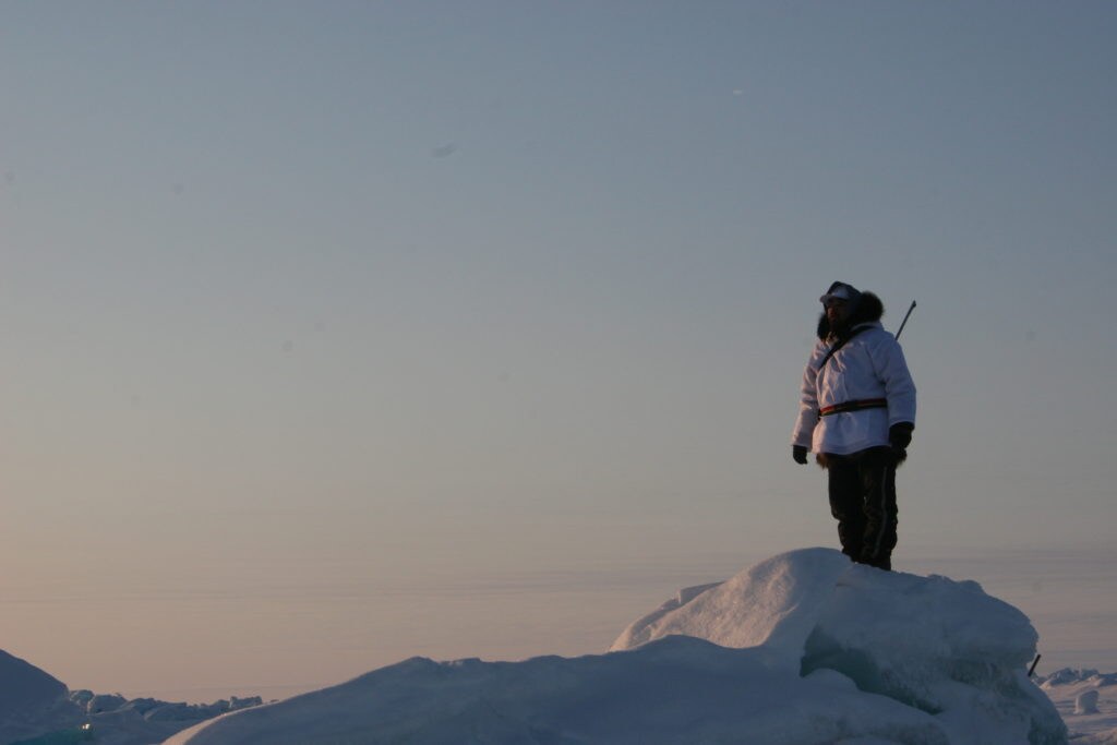 Lone person atop a peak of ice looking out over the Arctic sea ice.