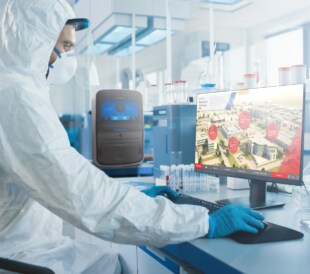 Scientist in clean room suit and mask sitting at work table with computer logged into portal