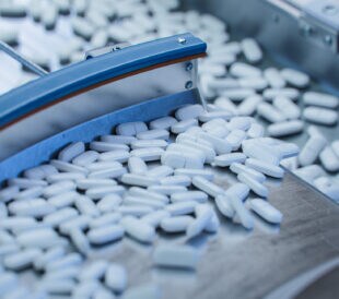 Tablets and Capsules Manufacturing Process. Close-up Shot of Medical Drug Production Line. White Painkiller Pills are Moving on Conveyor at Modern Pharmaceutical Factory.