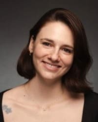 Headshot of a woman smiling with shoulder-length brown hair against a neutral background.