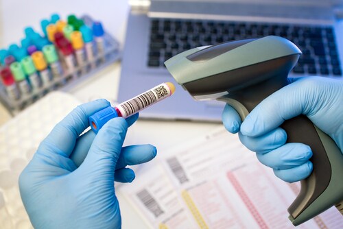 Technician hands scanning bar codes on biological sample tube in the lab of blood bank. Image: angellodeco/Shutterstock.com.