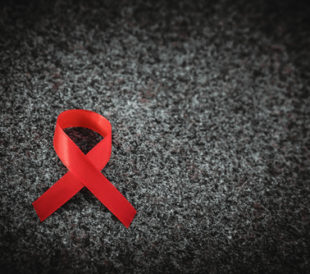 Red ribbon on granite, black and white, World AIDS Day concept. Image: Alexxndr/Shutterstock.com.