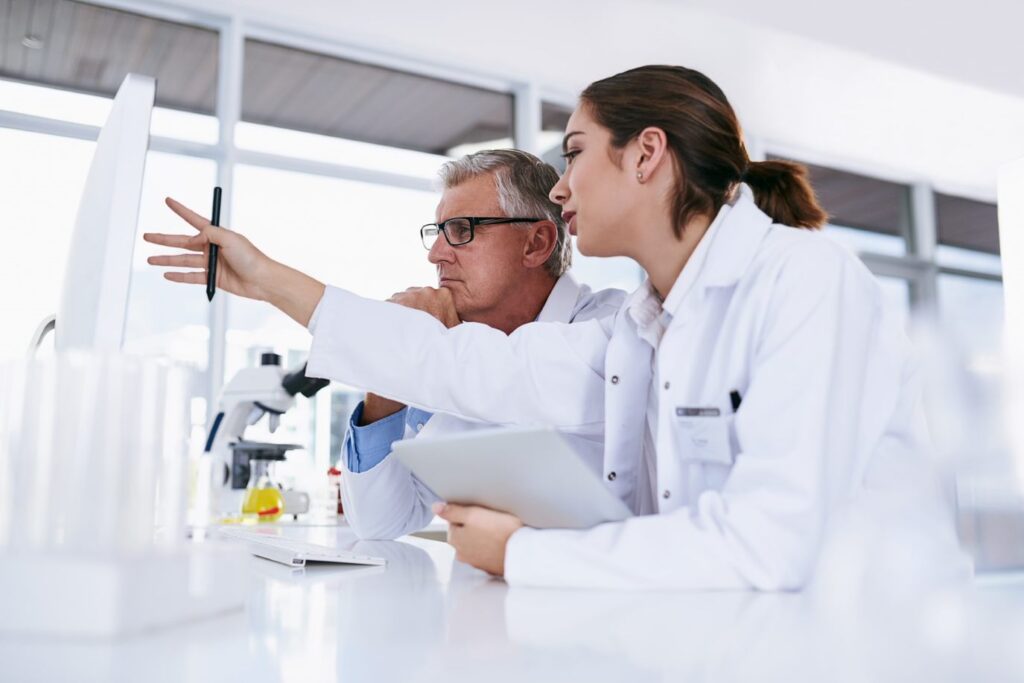 Male and female scientists working in a lab. Female scienist is pointing at computer screen.