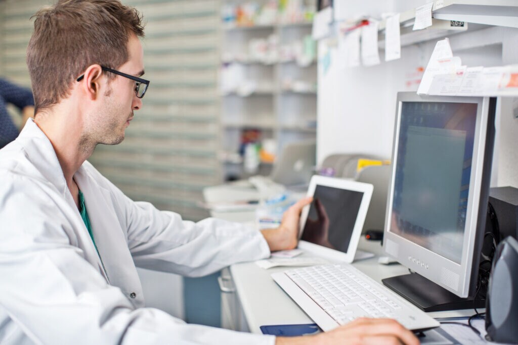 Male scientist in biotech lab working on a computer and tablet using eProcurement Manager software. 