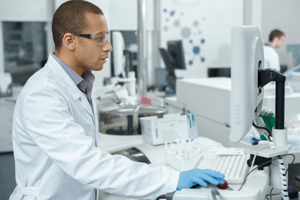 Scientist working at a computer in a laboratory wearing safety glasses. 
