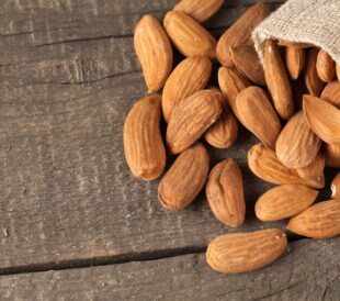 Raw almonds spilling out of a burlap bag onto a wooden background