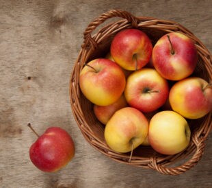 Red and yellow apples in a basket on a wooden table