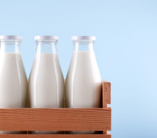 Three glass milk bottles in a wooden crate on a blue background