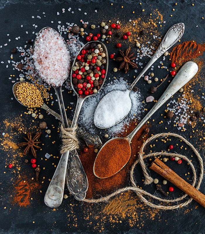 Commonly fraudulent herbs and spices sit in spoons on a black table