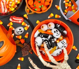 Halloween trick or treat scene with jack o lantern pails and a variety of candy. Top view on a black background.