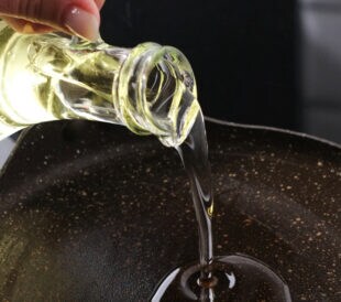 Girl Drizzling Oil Into A Heated Pan