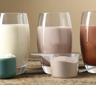 Different tasty protein cocktails in glasses and powders on wooden table