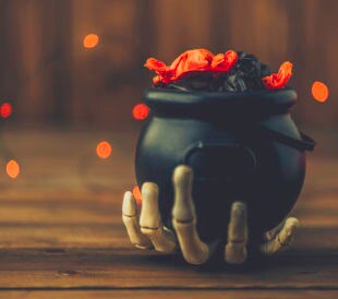 Halloween background with cauldron, candy and skeleton hand