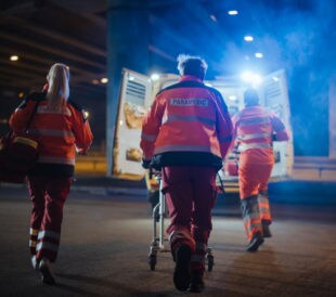 Team of EMS Paramedics React Quick to Provide Medical Help to Injured Patient and Get Him in Ambulance on a Stretcher. Emergency Care Assistants Arrived on the Scene of a Traffic Accident on a Street.