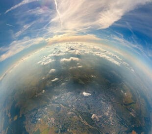 Aerial view from airplane window at high altitude of little planet distant city covered with layer of thin misty smog and distant clouds in evening.