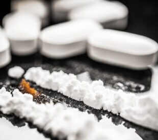 A close-up view of white pills alongside fentanyl powder, emphasizing the relationship between prescription drugs and the opioid crisis affecting many individuals in society.