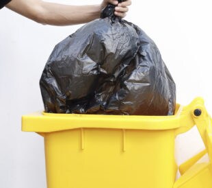 plastic trashbag being put in outdoor barrell