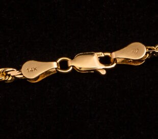 Clasp on a 14k Gold necklace with markings on a black background