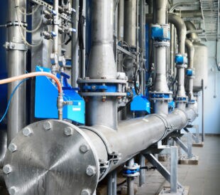 Large industrial water treatment and boiler room. Shiny steel metal pipes and blue pumps and valves.