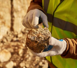 Close up of industrial worker holding mineral ore in gloved hands on mining site