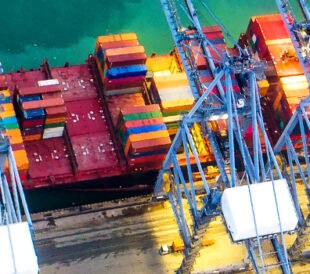 Red commercial boat floating in teal blue water, transporting shipping containers