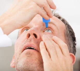 man putting drops in his eye