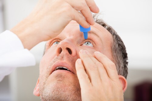 man putting drops in his eye