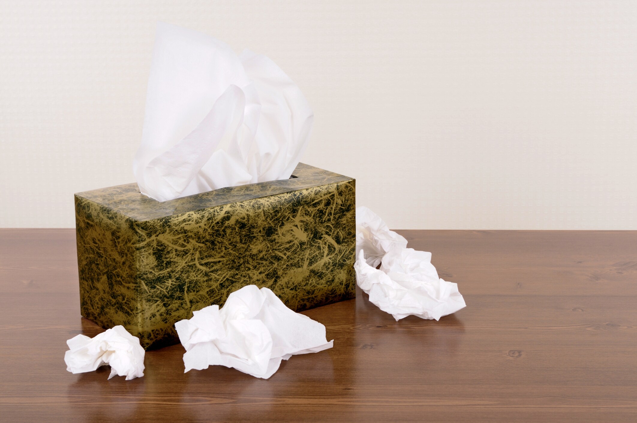 Box of tissues on a wood table (the background is cream pattern wallpaper).