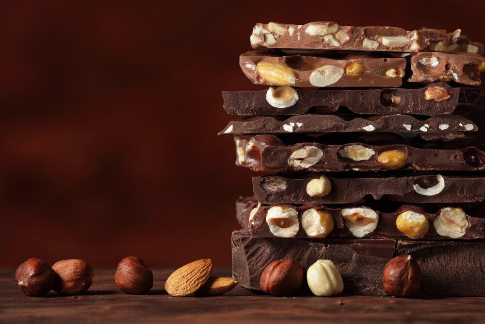 Light and dark chocolate bars with nuts layered on a brown background