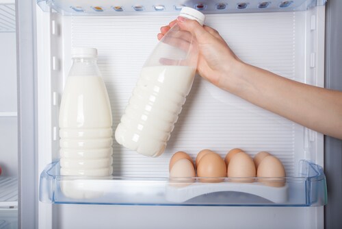 A hand reaches into a fridge to grab one of two milk bottles that are next to a dozen eggs. Image: takoburito/Shutterstock.com