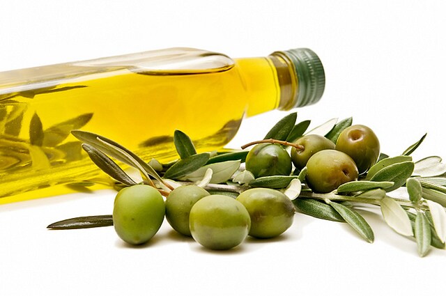 A bottle of olive oil lies on its side behind a branch of green olives
