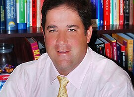 Dr. Andrew Brooks looks at the camera in front of a wall of books.