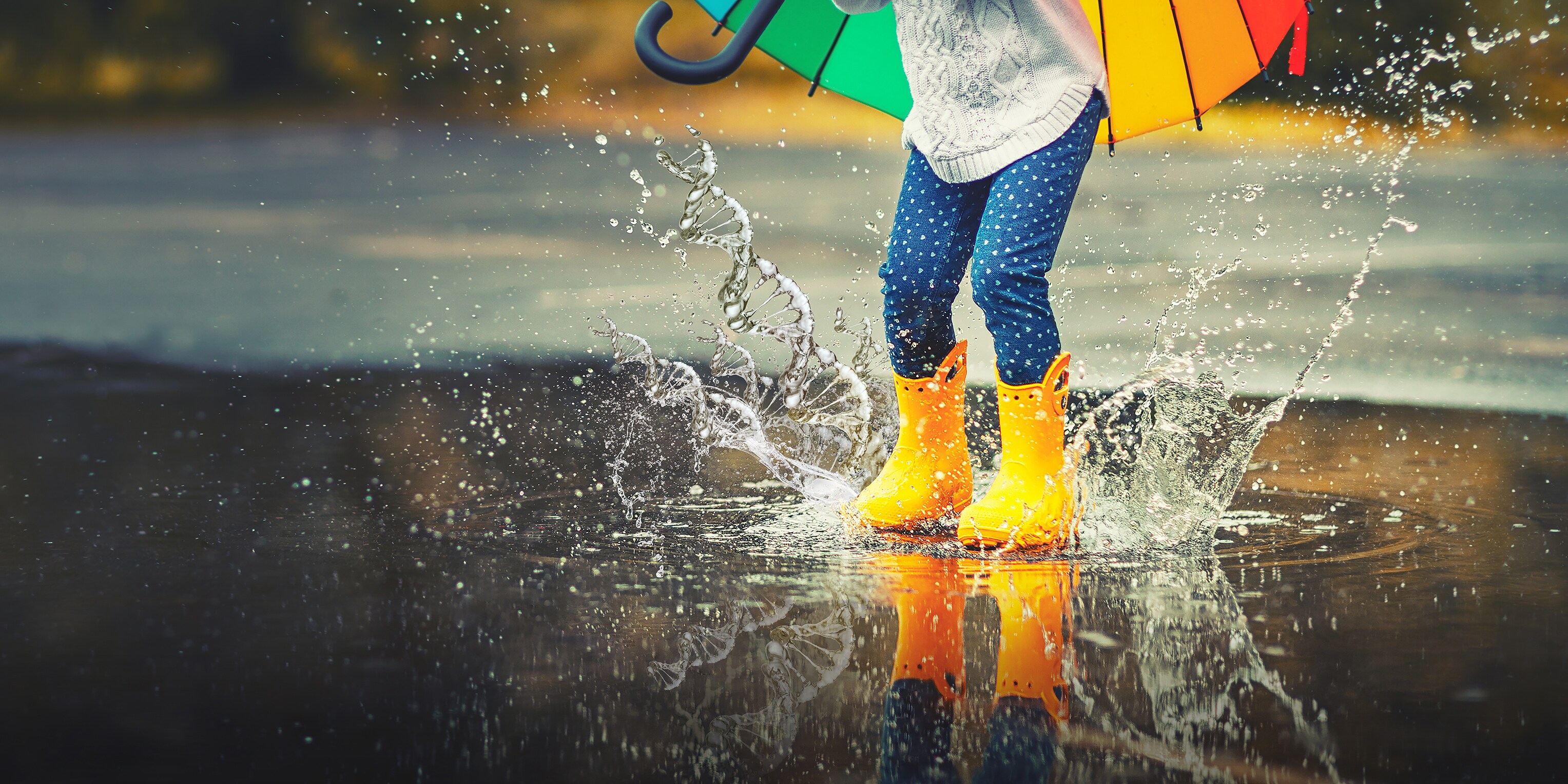 A child in yellow rain boots jumps into a puddle