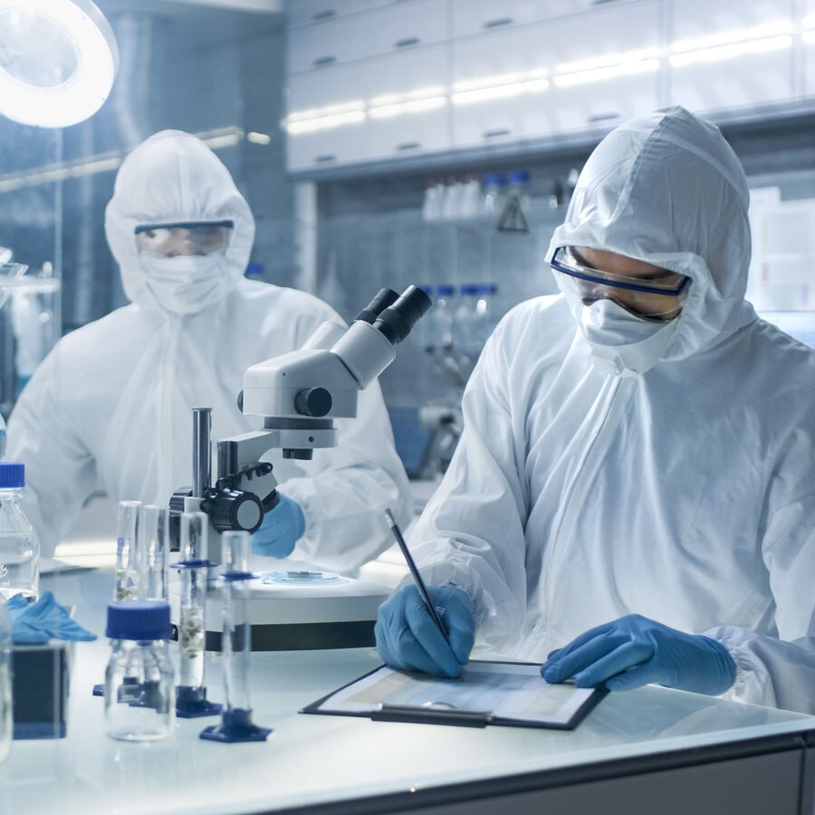 Lab workers write on clipboard at lab bench Two lab workers in PPE discuss and record information together at the bench in a secure lab