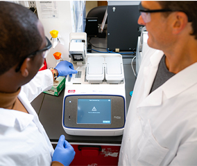 Thermal Cycler Service Plans Two scientists in lab coats are looking down at a PCR thermal cycler, inputting tubes into one of three blocks
