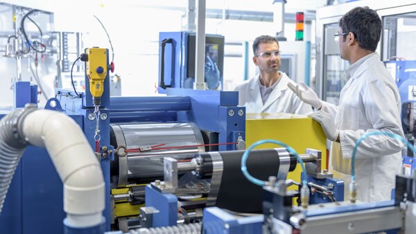 Two scientists wearing protective eye wear and white lab coats, talking in a Lithium-Ion battery production line Two scientists wearing protective eye wear and white lab coats, talking in a Lithium-Ion battery production line